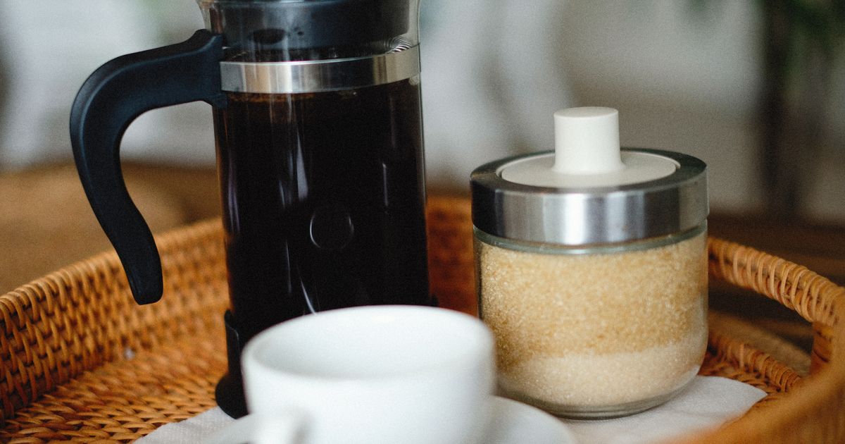 A French press, a cup of black coffee and a sugar jar on a tray