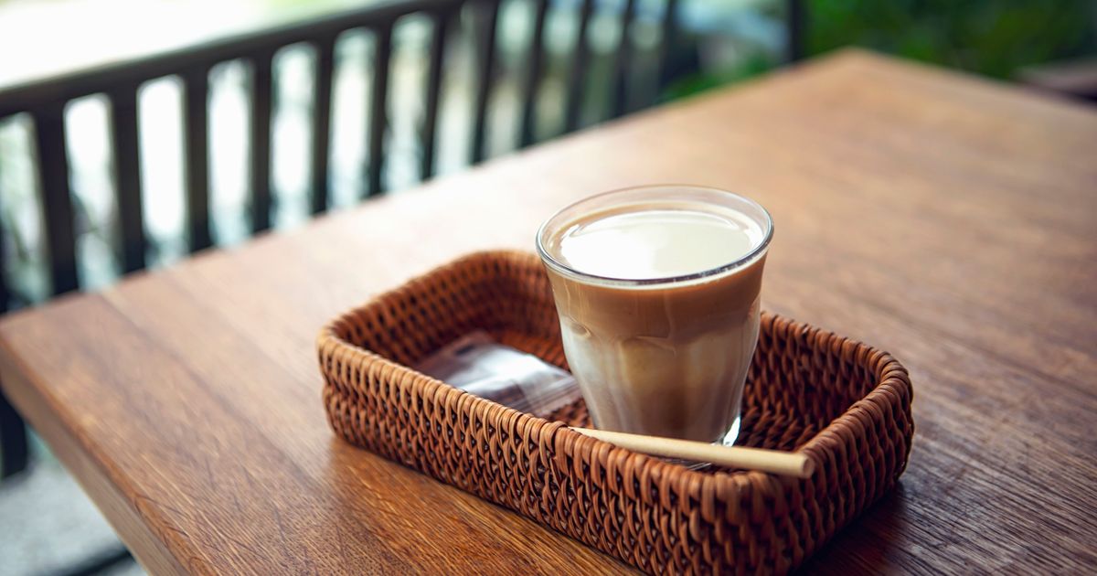 A latte in a glass in a woven basket on a wooden table