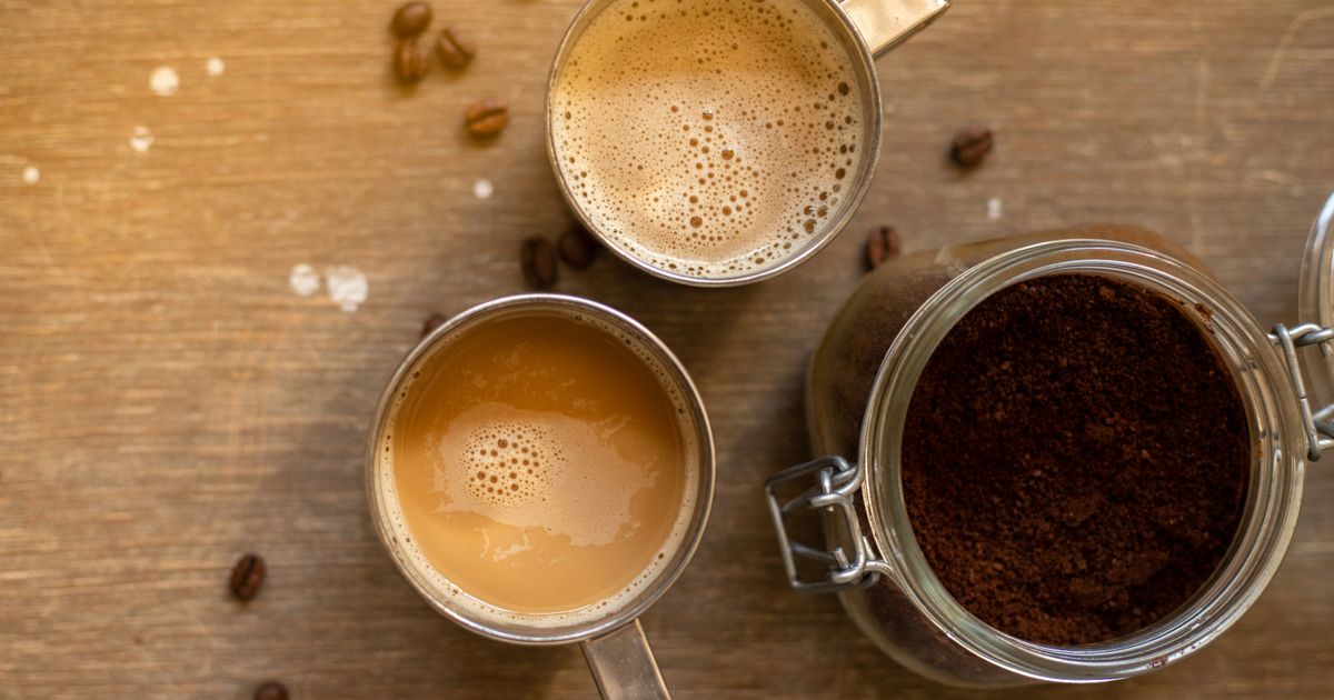 Two cups of milky coffee beside a jar of ground coffee