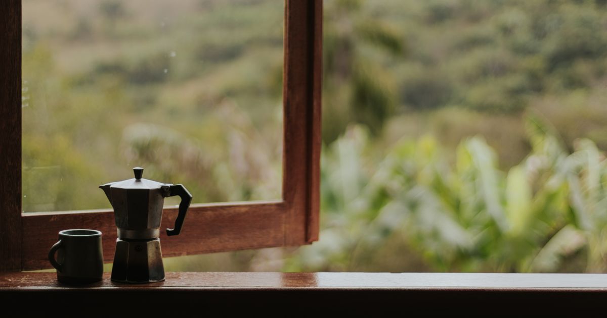 A coffee pot and a cup of coffee on a window sill in the morning