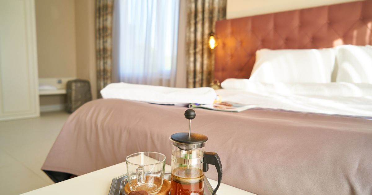 A French press of coffee on a bedside table next to a bed