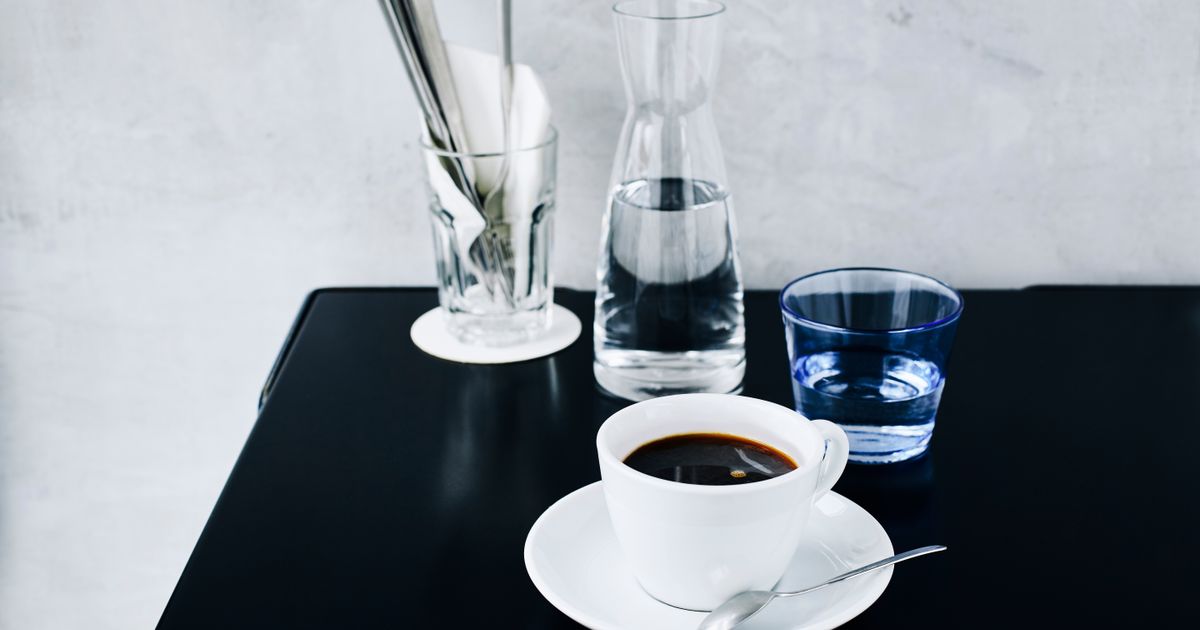 A cup of black americano coffee with a glass of water on a dark café table