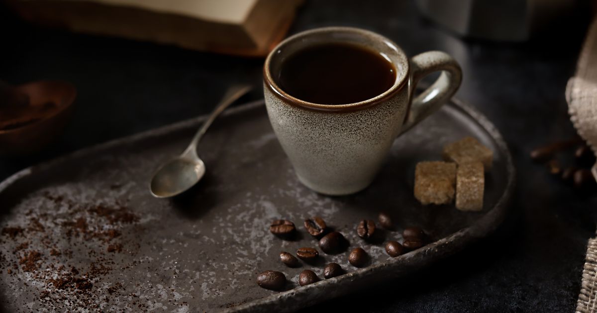 A cup of black coffee with sugar cubes and coffee beans