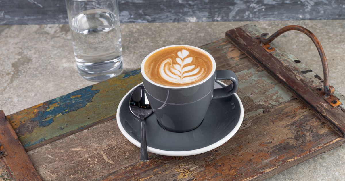 A milky coffee with latte art on a saucer beside a glass of water