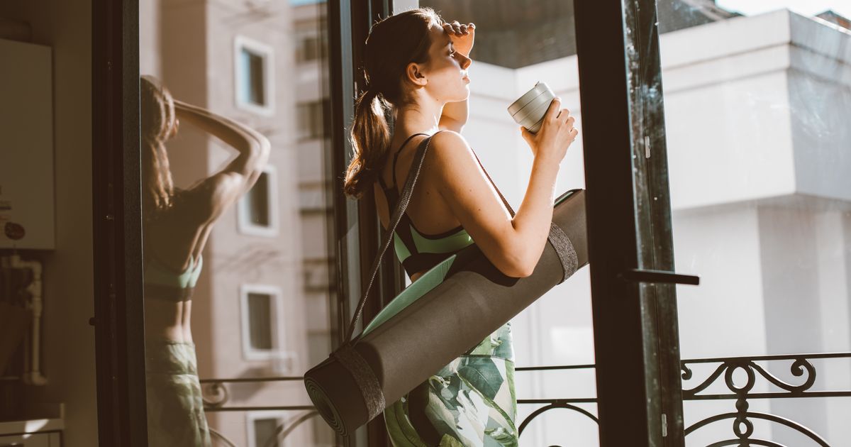 A woman in workout clothes holding a cup of coffee and a yoga mat