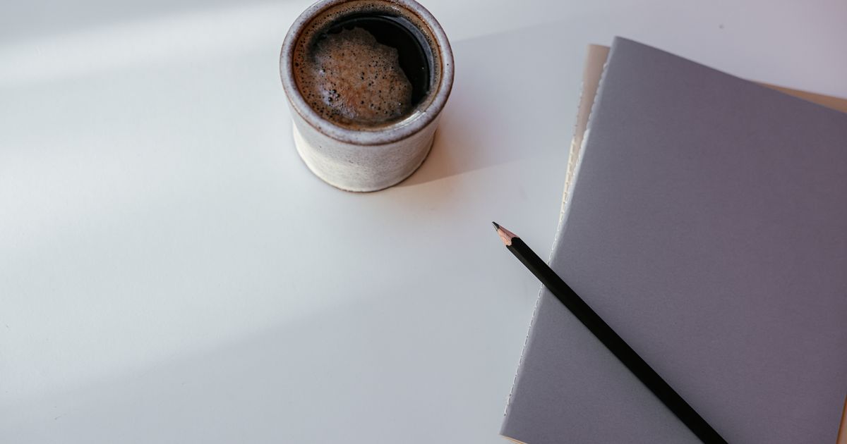 A mug of black coffee beside a notebook and pen on a white desk