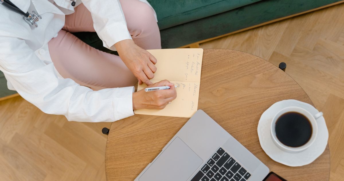 A doctor writing notes at a desk beside a cup of black coffee